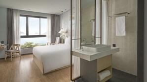 A modern hotel room with a large bed, a bedside table with a lamp, a bathroom with a large mirror, and a view of the sea. - The Secret Con Dao (Ho Chi Minh City)