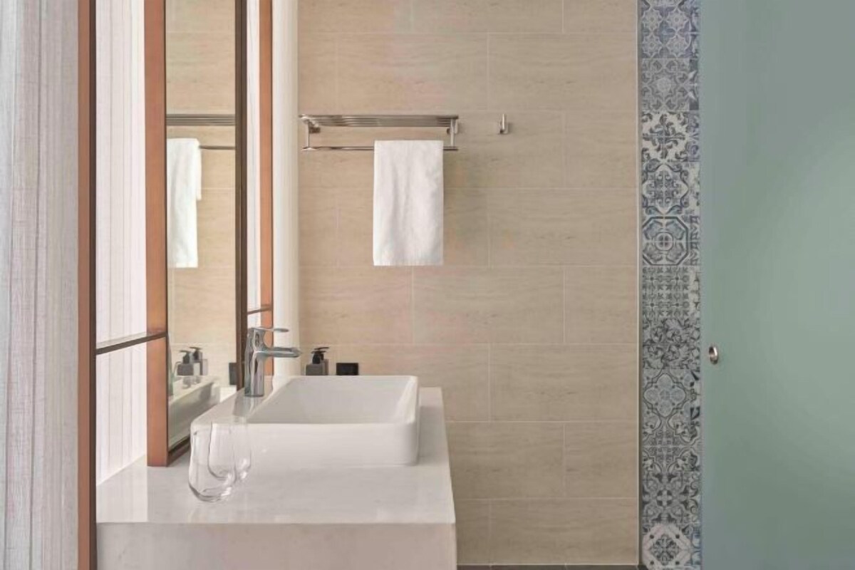 A modern bathroom with a large mirror, a white sink, and a towel rack.