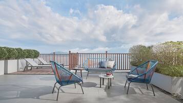 Une terrasse extérieure avec deux chaises bleues en fil de fer, un canapé gris et une petite table ronde.