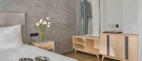 A modern hotel room with a large bed, a bedside table with a vase of flowers, a wooden dresser, and a mirror.