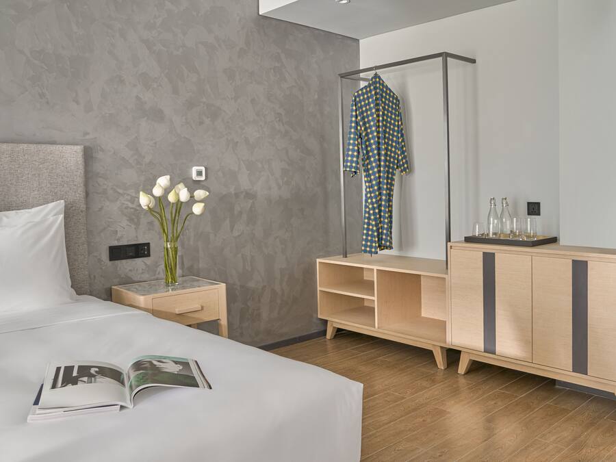Una habitación de hotel moderna con una cama grande, una mesita de noche con un florero, un aparador de madera y un espejo.