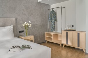 Une chambre d’hôtel moderne avec un grand lit, une table de chevet ornée d’un vase de fleurs, une commode en bois et un miroir.