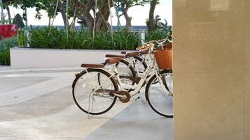 A row of bicycles parked in an outdoor area with a tiled floor and a planter with green plants in the background.