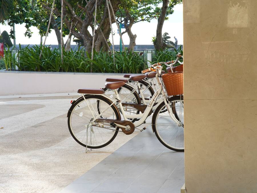 A row of bicycles parked in an outdoor area with a tiled floor and a planter with green plants in the background.