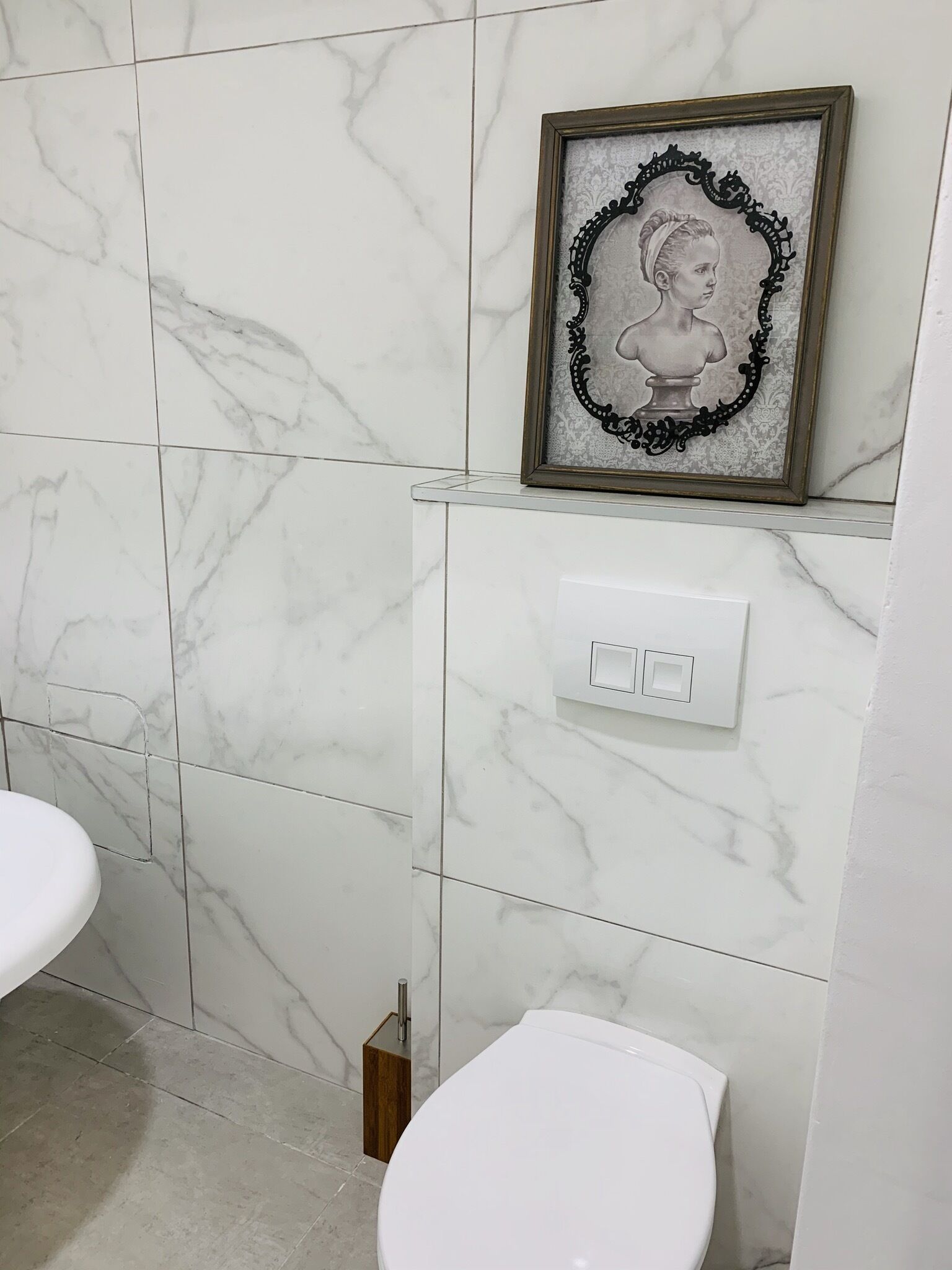 A bathroom with white marble tiles, a framed portrait, a white toilet, and a wooden cabinet.