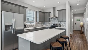 Una cocina moderna con gabinetes grises, un refrigerador de acero inoxidable, una isla grande con taburetes y un salpicadero de azulejos.