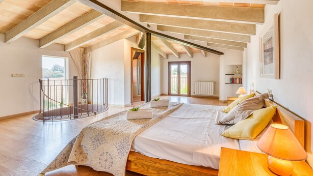 Un dormitorio amplio con una cama grande, un cabecero de madera y vistas al exterior a través de una puerta.