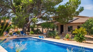 Una piscina con sillones de descanso, rodeada de plantas en macetas y árboles.