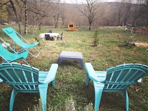 Ein Garten mit zwei türkisfarbenen Adirondack-Stühlen, einem kleinen Tisch und einem hölzernen Spielhäuschen.