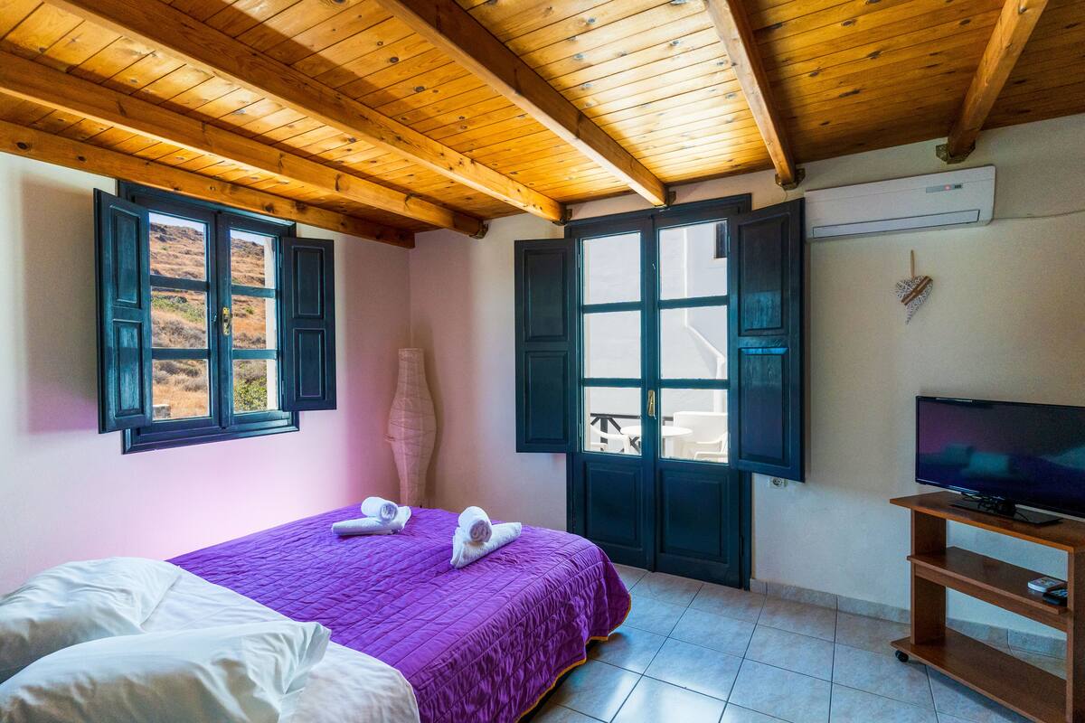 A bedroom with a bed, a television, and a window with a view of the outdoors.