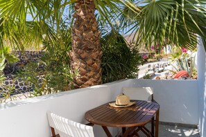 A wooden table and white chair on a balcony with a palm tree and plants.