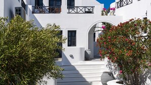 A white-walled building with a staircase leading to an entrance, surrounded by greenery and a clear blue sky. - Soulis Hotel (Santorini)