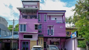 Ein mehrstöckiges Gebäude mit violetten Fassade, einer Garage mit geparkten Fahrzeugen und einem Schild.