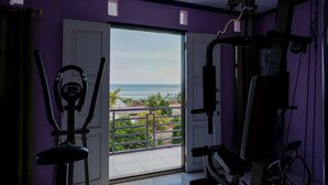 Ein Fitnessraum mit Trainingsgeräten und Meerblick durch eine Tür.