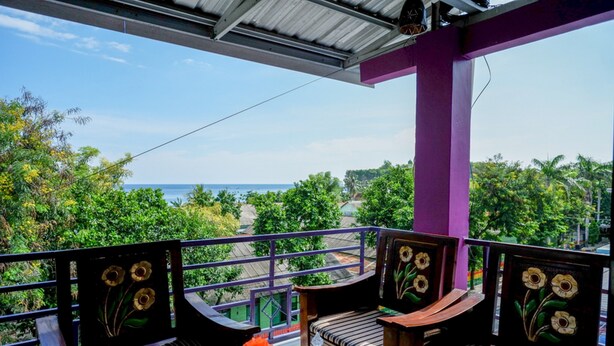 Ein Balkon mit zwei Holzstühlen und einem Tisch, mit Blick auf eine üppige grüne Landschaft und das Meer.