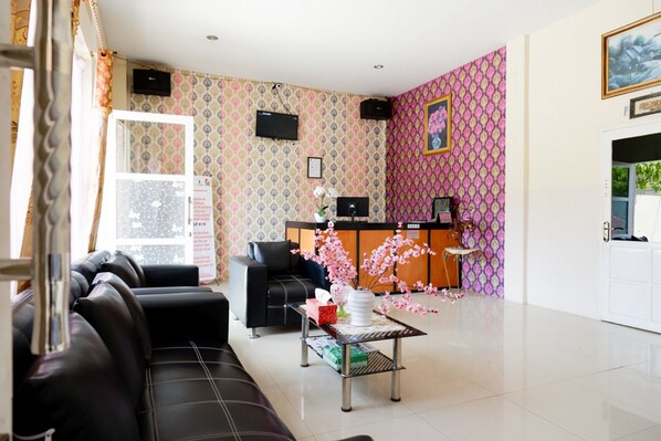 A hotel lobby with a reception desk, black leather sofas, a coffee table with a vase of flowers, and patterned wallpaper. - RedDoorz @ Hotel Grand Aulia Majene (Majene)