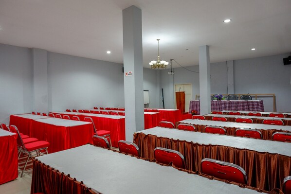 Un salón de conferencias con varias mesas y sillas, un candelabro y una zona de escenario.