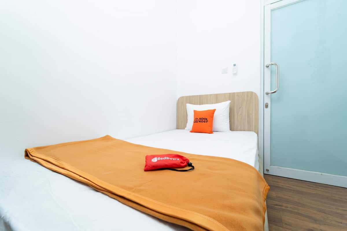 Ein Hotelzimmer mit einem Bett, einem Holz-Kopfteil, einer weißen Wand, einer hellblauen Tür und einem roten Kissen mit Text.