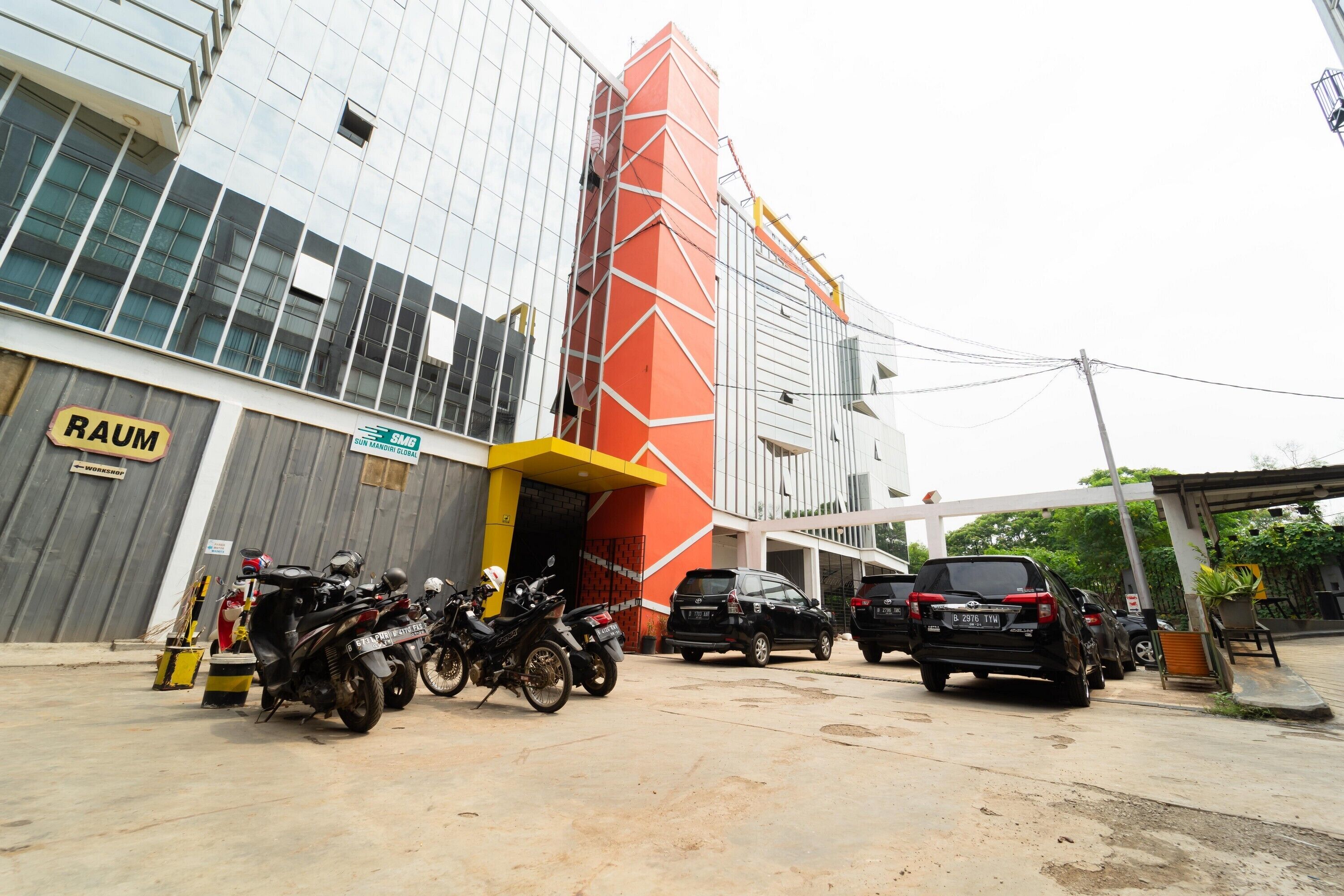 Un edificio de diseño moderno, con fachada de vidrio y un llamativo patrón geométrico rojo y blanco en el lateral. Varias motocicletas están estacionadas frente al edificio, y también se ven algunos automóviles.