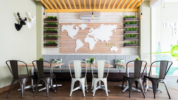 A restaurant with a wooden wall, world map, and plants. There are four chairs and a table. - RedDoorz Plus @ Harvest Inn Panakkukang (Makassar)