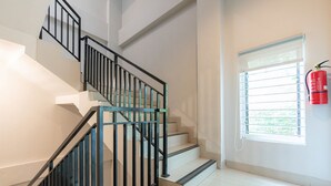 A staircase with black railings and a fire extinguisher mounted on the wall near a window. - RedDoorz Plus @ Harvest Inn Panakkukang (Makassar)