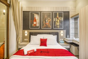 Una habitación de hotel con una cama, una mesita de noche, un escritorio y un espejo. Hay tres cuadros enmarcados en la pared sobre la cama.