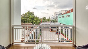 Un balcón con vistas a una calle, un edificio de fachada verde y un suelo de baldosas.