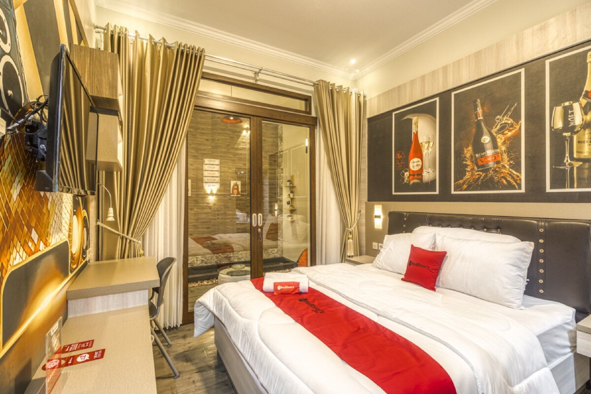 Habitación de hotel con cama, escritorio, silla, televisión y puerta de vidrio que da a un balcón.