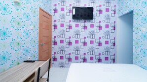 A room with a bed, a desk, a chair, a TV mounted on the wall, and a door. - KoolKost @ Menceng Raya (Jakarta)