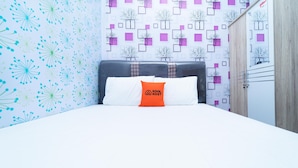 A hotel room with a bed, a pillow with a logo, a patterned wall, and a wardrobe. - KoolKost @ Menceng Raya (Jakarta)