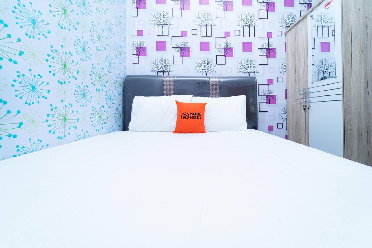 Una habitación de hotel con cama, almohada con logotipo, pared con diseño y armario.