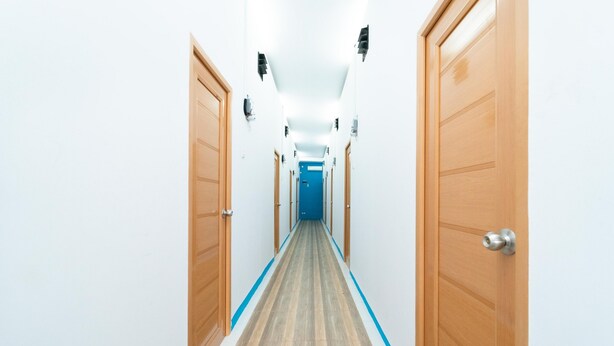 A long, narrow hallway with wooden doors on both sides, leading to a blue door at the end. - KoolKost @ Menceng Raya (Jakarta)