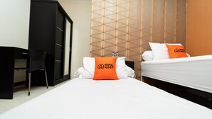 A hotel room with a bed, a desk, and a wardrobe. There are two pillows with the hotel's logo. - KoolKost Syariah near TerasKota BSD (South Tangerang)