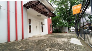A building with a red and white facade, a brick-paved courtyard, and a signboard. - KoolKost Syariah near TerasKota BSD (South Tangerang)