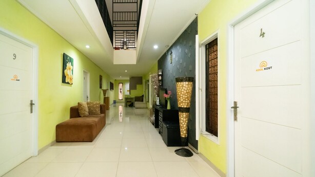 A hotel hallway with a brown sofa, a black cabinet, and a white door with a logo. - KoolKost Syariah near TerasKota BSD (South Tangerang)