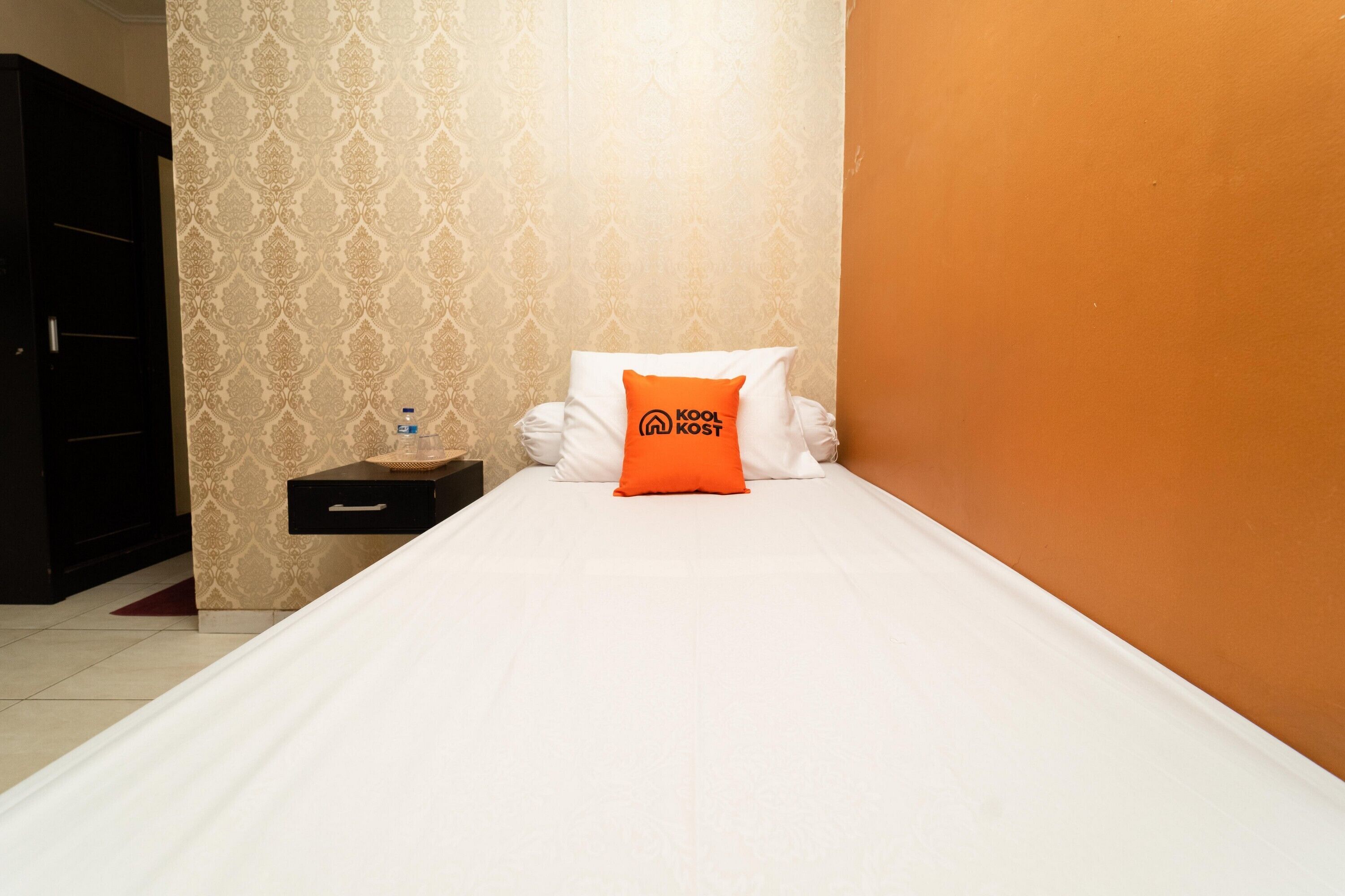 Ein Hotelzimmer mit Bett, Nachttisch, Wasserflasche und Kopfkissen mit Logo.