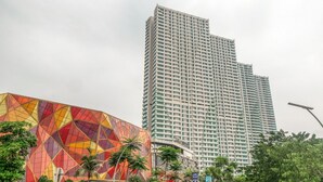 A tall, modern building with a grid-like facade and a colorful, geometric structure in the foreground. - RedLiving Apartemen Grand Kamala Lagoon - Kita Pro Tower Barclay North (Bekasi)