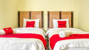 Two twin beds with red and white bedding, a wooden headboard, and a red pillow with the RedDoorz logo. - RedDoorz @ Jalan Kapten Muslim Medan (Medan)