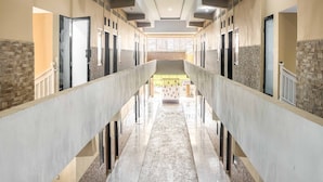 A hotel corridor with a central staircase, multiple doors, and a tiled floor. - RedDoorz @ Jalan Kapten Muslim Medan (Medan)