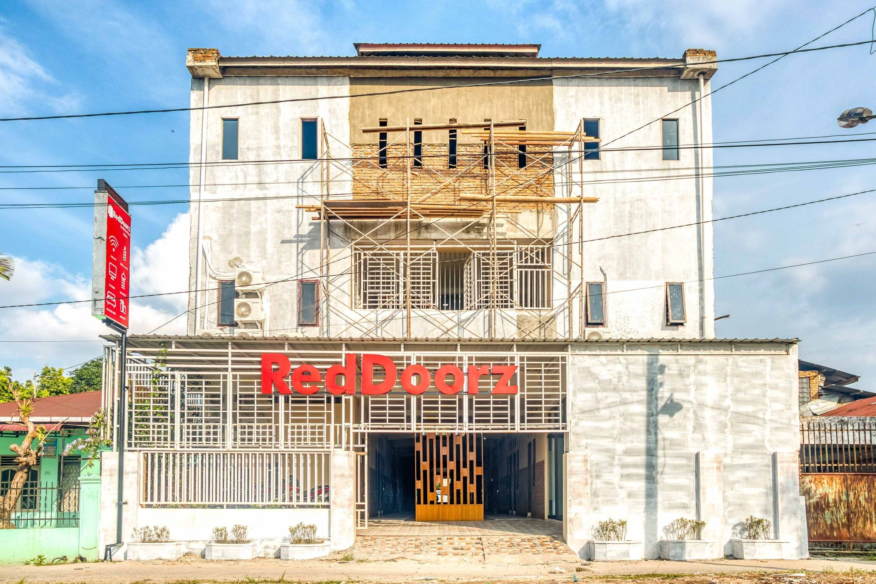Un edificio con un letrero que dice "RedDoorz" y un letrero rojo a la izquierda.