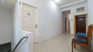 A hallway with a white door marked '12', a wooden chair, and a blue cabinet. - RedDoorz Syariah near Stasiun Kereta Api Kisaran (West Kisaran)