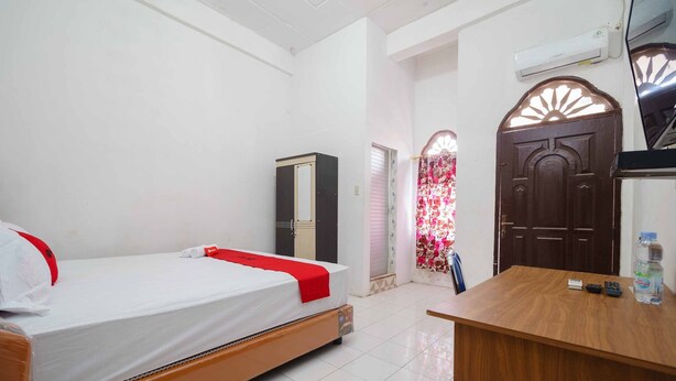 A hotel room with a bed, a wooden desk, an air conditioner, and a wardrobe. - RedDoorz Syariah near Stasiun Kereta Api Kisaran (West Kisaran)