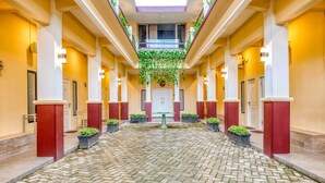 A hotel lobby with a central open space, columns, and potted plants. - RedDoorz Syariah near Kebon Rojo Park Blitar (Blitar)