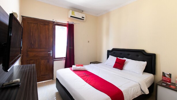A hotel room with a bed, a TV on a wooden table, and an air conditioning unit on the wall. - RedDoorz @ Raya Janti Yogyakarta (Baturetno)