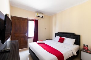 A hotel room with a bed, a TV on a wooden table, and an air conditioning unit on the wall. - RedDoorz @ Raya Janti Yogyakarta (Baturetno)