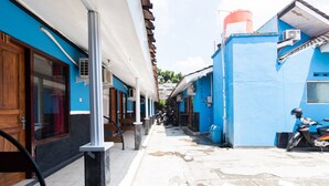 A narrow street with buildings on either side, a scooter parked on the right, and a wooden door on the left. - RedDoorz @ Raya Janti Yogyakarta (Baturetno)