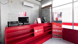 A reception area with a red desk, a computer, and a RedDoorz advertisement. - RedDoorz @ Raya Janti Yogyakarta (Baturetno)