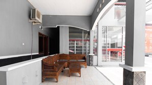 A spacious lobby with a wooden bench seating area, a tiled floor, and a large glass door leading outside. - RedDoorz @ Raya Janti Yogyakarta (Baturetno)