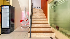 Una escalera con barandilla de vidrio, una máquina expendedora y una silla con cojín rojo.