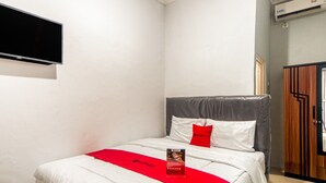 Una habitación de hotel con cama, una colcha roja y blanca, almohada, televisor montado y armario de madera.